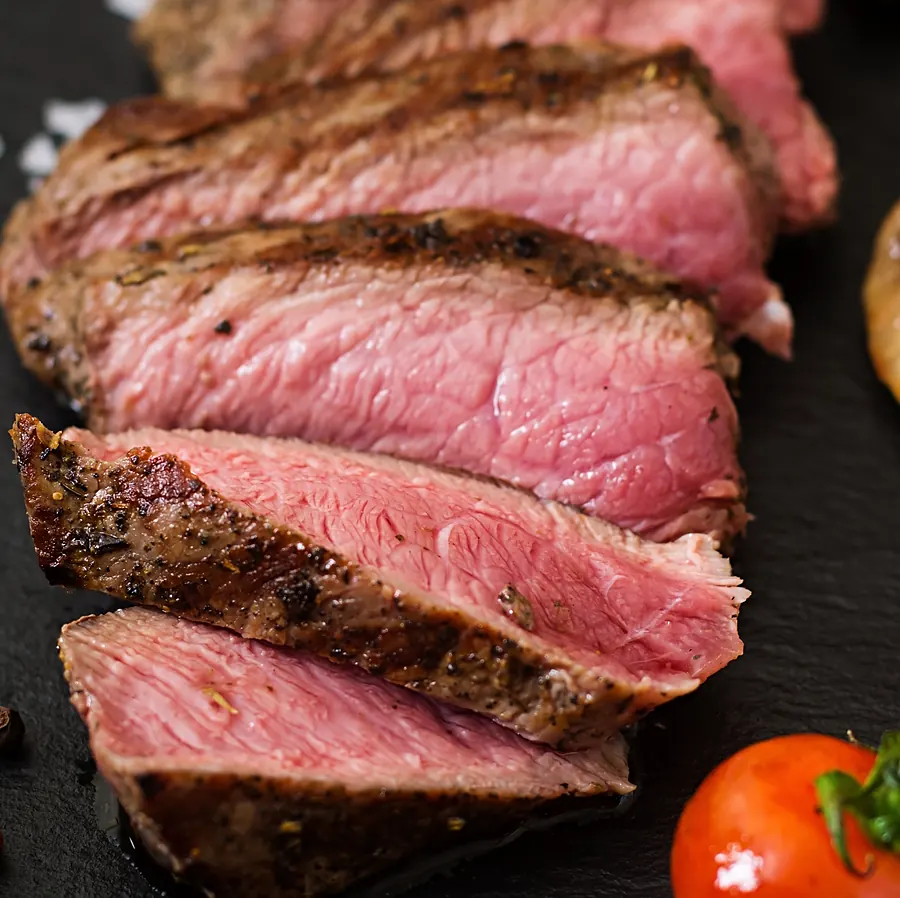 Carne grelhada fatiada, rosada por dentro, sobre pedra escura